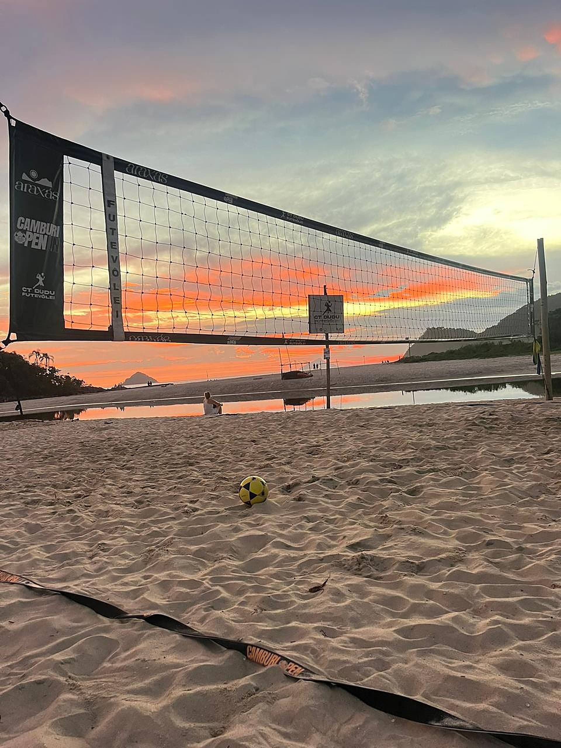 Quadra do CT Dudu Futevôlei com rede e bola na areia durante o pôr do sol